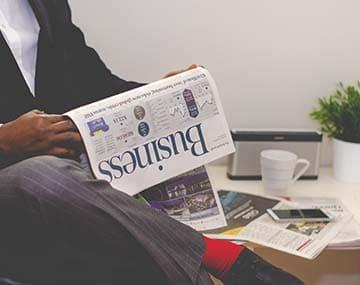 A business immigration person in a grey suit is reading the business section of the newspaper.